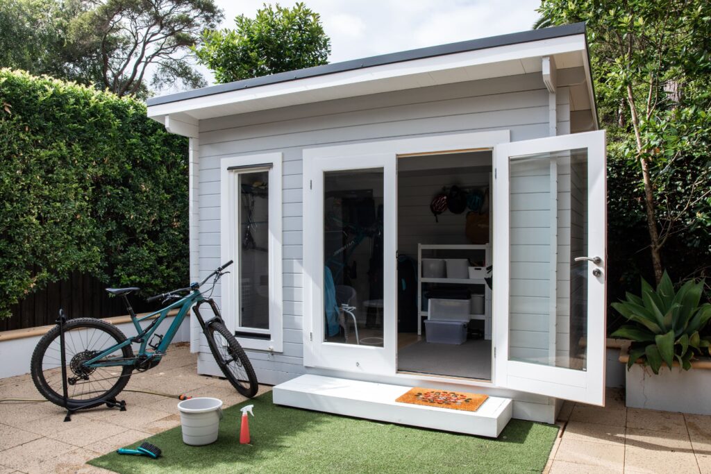 Ein modernes Gartenhaus mit einem Fahrrad davor, das an einem Fahrrad Anlehnbügel sicher abgestellt ist, umgeben von gepflegter Gartenlandschaft.