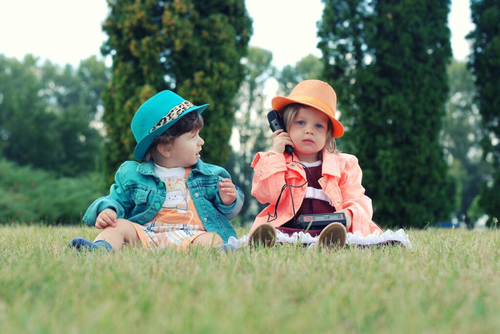 Zwei Kinder in bunter Kleidung und Hüten sitzen auf einer Wiese, eines hält ein altes Telefon. Perfekt, um Dias digitalisieren und diese wertvollen Kindheitserinnerungen zu bewahren.