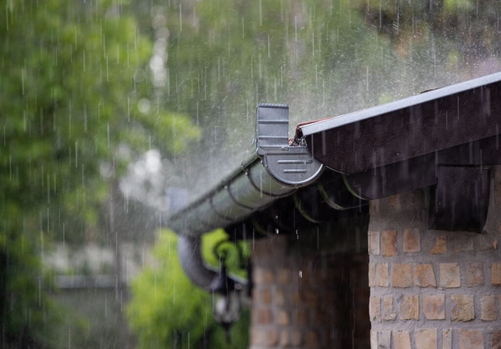 Regenwasser fließt von einem Hausdach in eine Dachrinne zur Speicherung in einer Zisterne für die Gartenbewässerung