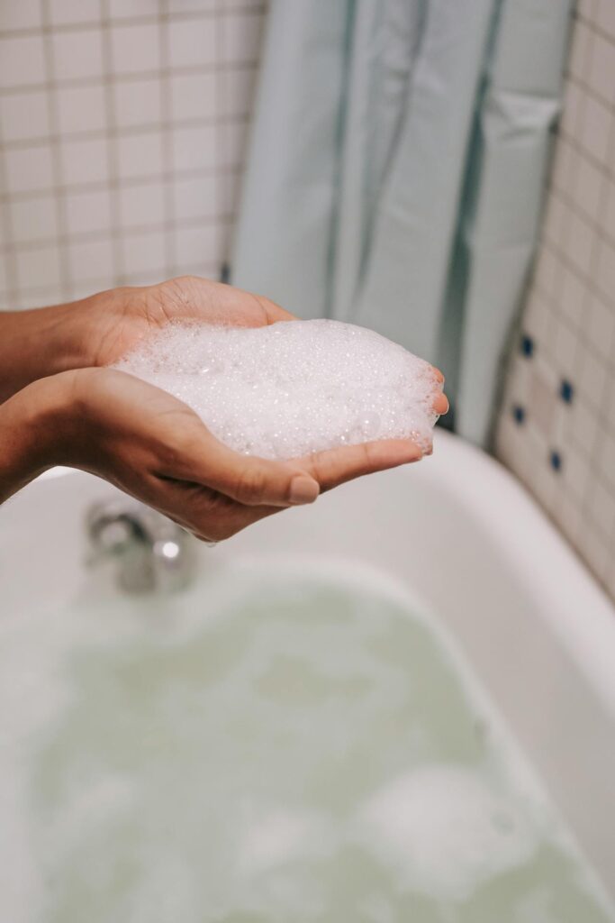 Hände, die Schaumbad in einem Badezimmer halten, ausgestattet mit einem Durchlauferhitzer für die Dusche, der eine energieeffiziente und sofortige Warmwasserversorgung bietet.