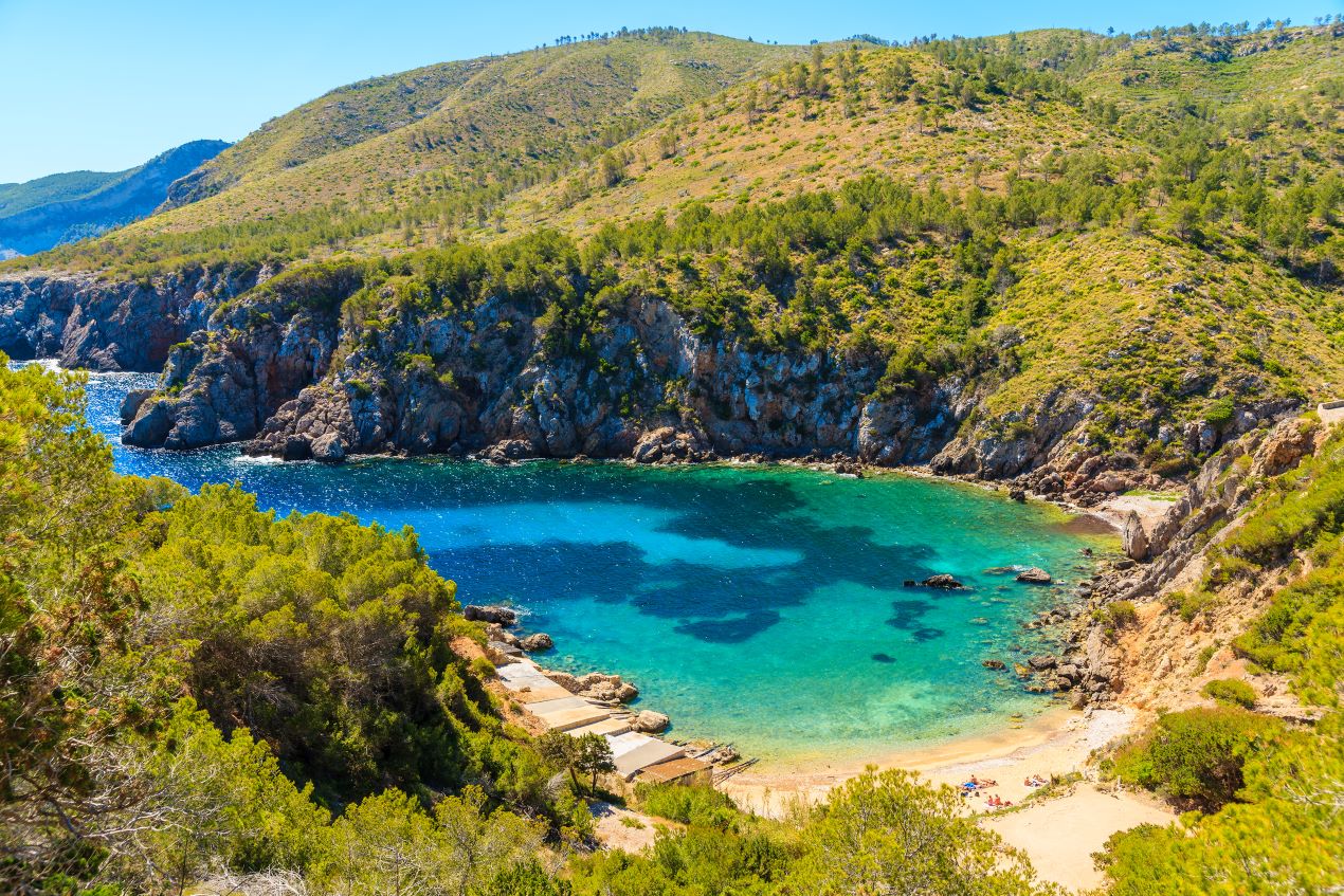 Traumhafte Bucht mit kristallklarem Wasser und grünem Hinterland auf Ibiza – perfekt für eine Auszeit nach einem Ibiza Restaurant Geheimtipp.