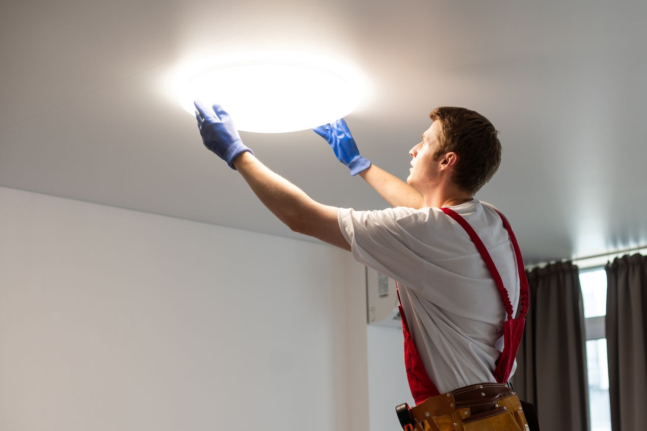 Ein Handwerker bei der Installation einer Deckenleuchte mit LED E27-Lampe, die eine helle und gleichmäßige Beleuchtung im Raum erzeugt.