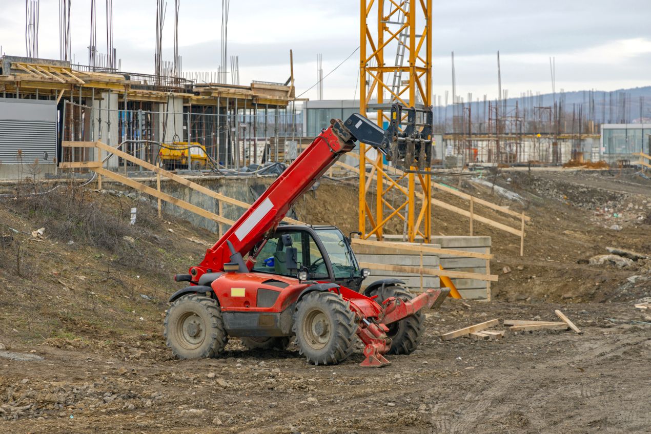 Ein roter Teleskopstapler hebt Baumaterial auf einer Baustelle – eine typische Anwendung für alle, die einen Teleskopstapler mieten möchten